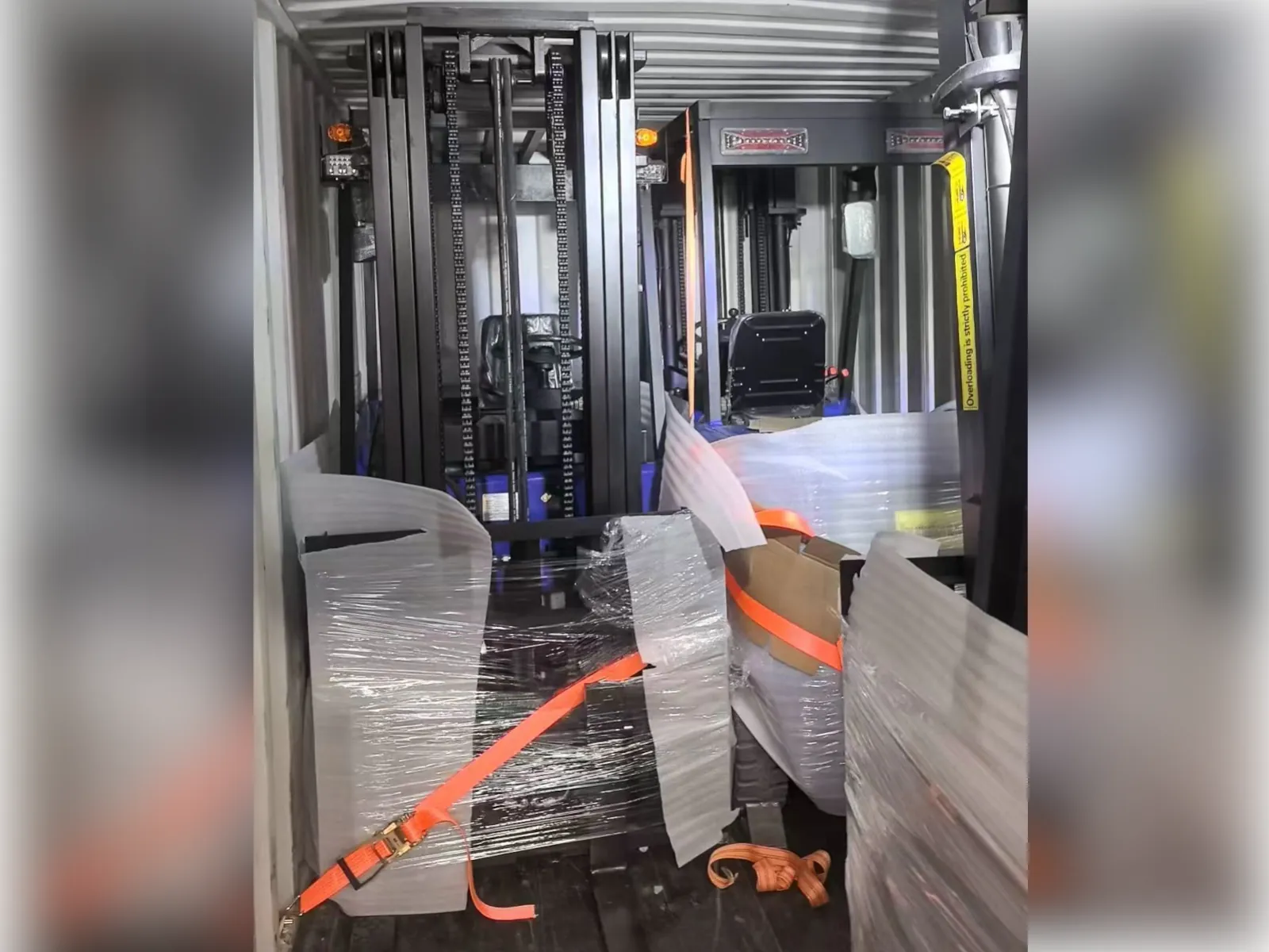 Inside a shipping container showing three forklifts securely strapped and ready for transport
